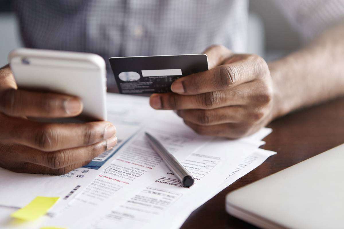 Online payment and shopping concept. Cropped shot of African-American male holding cell phone in one hand and credit card in other, making transaction Digital Debt Collections Trends